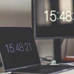 Laptop und Monitor an einem Arbeitsplatz zeigen eine digitale Uhrzeit