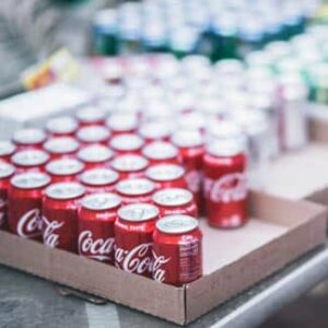 Mehrere rote Coca-Cola-Dosen stehen in offenen Kartons auf einem Tisch