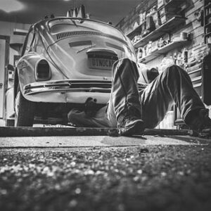 Schwarz-Weiß-Aufnahme einer Person, die in einer Werkstatt unter dem Heck eines Autos arbeitet