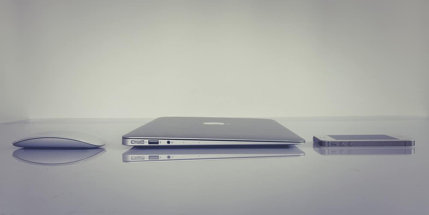 Geschlossenes MacBook zwischen Computermaus und Smartphone auf einer spiegelnden Oberfläche