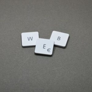 Drei weiße Buchstabensteine mit den Buchstaben W, E und B liegen auf einer dunklen Oberfläche