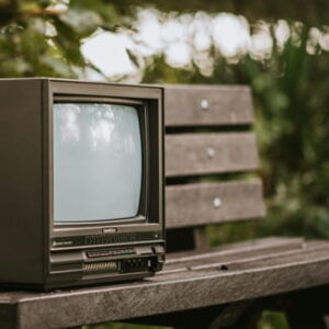 Alter Röhrenfernseher auf einer Holzbank im Freien mit unscharfer Vegetation im Hintergrund