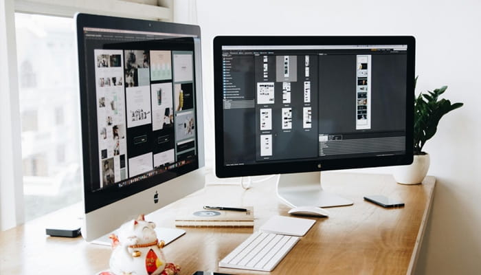 Arbeitsplatz mit zwei großen Monitoren, auf denen Entwürfe und Layouts für Webseiten geöffnet sind