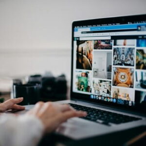 Person arbeitet an einem Laptop, auf dessen Bildschirm eine Übersicht mit verschiedenen Bildern geöffnet ist