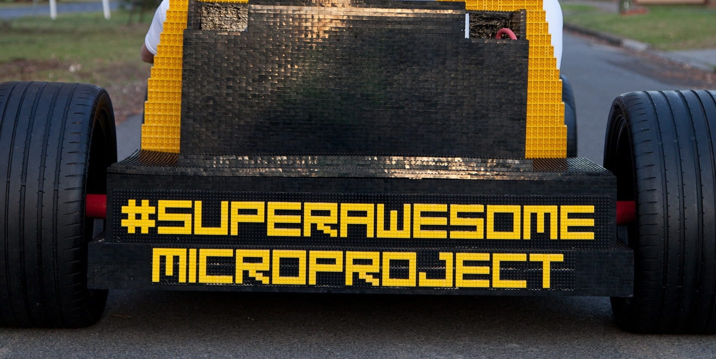 Unternehmenswebseite – Aufbau, Aufgaben und Verantwortung Heck eines schwarzen und gelben Fahrzeugs aus Klemmbausteinen mit der Aufschrift „#SUPERAWESOME MICROPROJECT“ zwischen zwei großen Reifen
