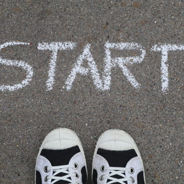 START Schriftzug auf Asphalt mit Schuhen als Symbol für den Neustart von 4Bullmann mit Divi 5