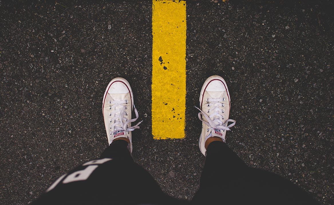 Person steht vor einer gelben Linie auf Asphalt als Symbol für Barrieren, Grenzen und barrierefreies Webdesign.