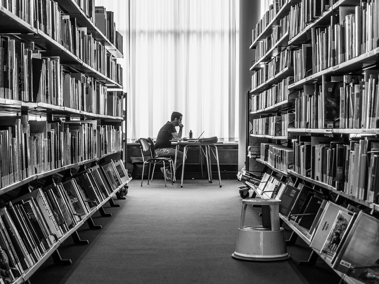 Person arbeitet zwischen hohen Bücherregalen als Symbol für Wissen und Inhalte, die Menschen, Suchmaschinen und KI aus einer Firmenwebseite erschließen