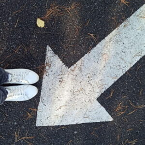 Weiße Turnschuhe stehen neben einem großen weißen Richtungspfeil auf dunklem Asphalt