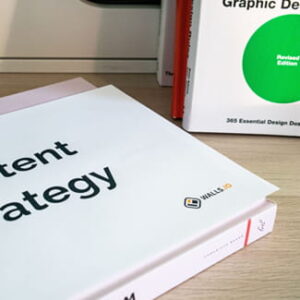 Ein Buch mit der Aufschrift „Content Strategy“ liegt auf einem Schreibtisch vor einem aufgestellten Buch über Grafikdesign