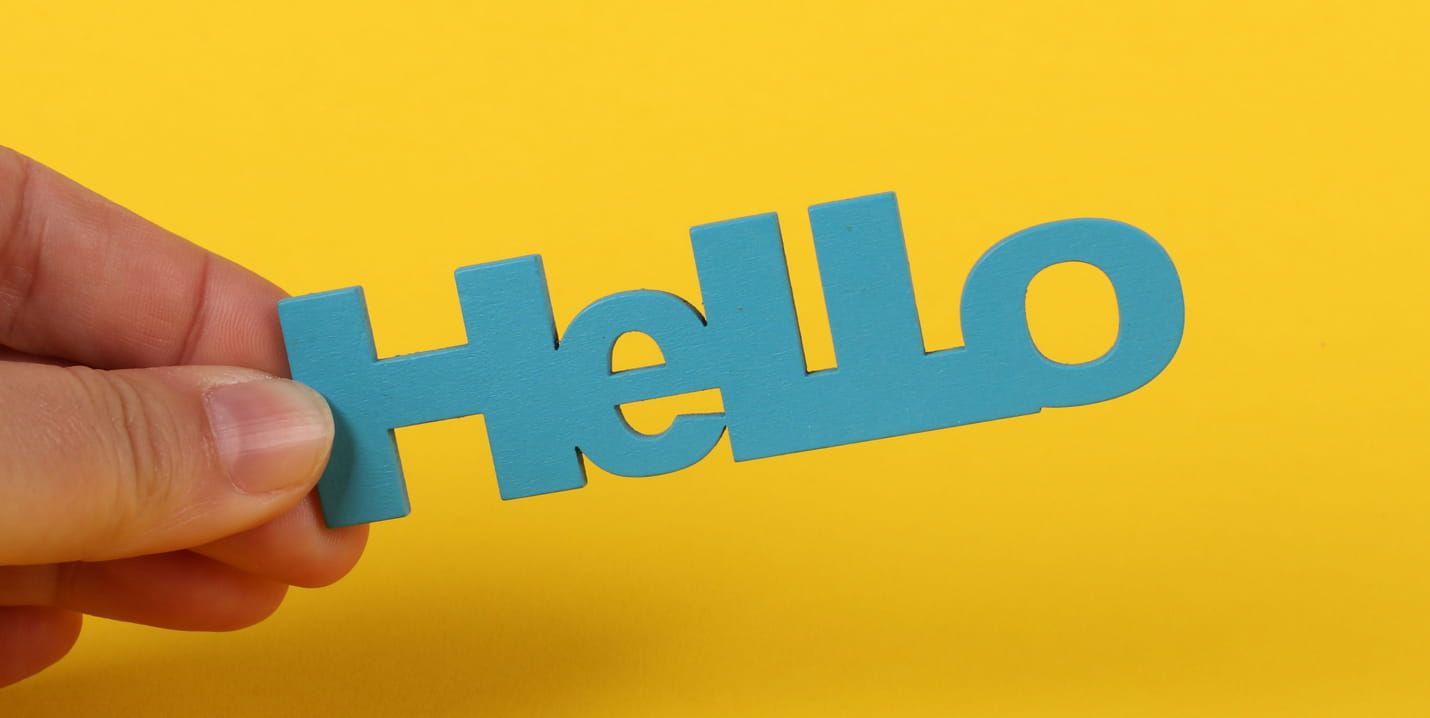 Hand hält einen blauen Hello-Schriftzug vor gelbem Hintergrund