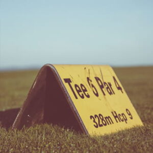 Gelbes Schild mit der Aufschrift „Tee 6 Par 4“ steht auf einem Golfplatz