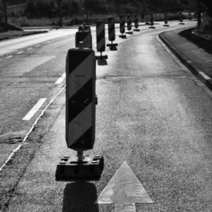Schwarz-Weiß-Aufnahme einer Straße mit Absperrbaken und einem weißen Richtungspfeil auf der Fahrbahn